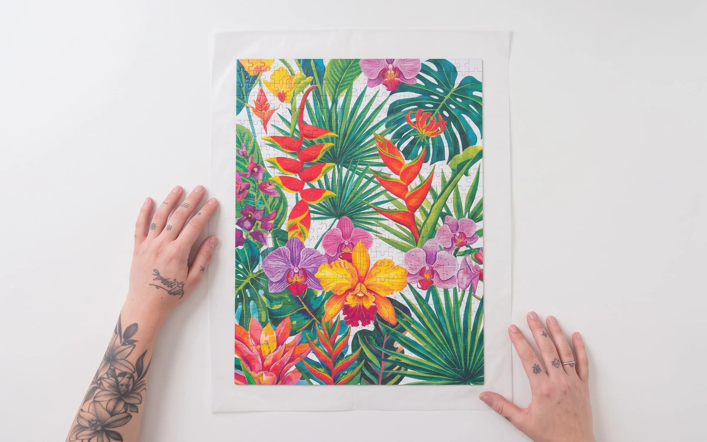 Vista superior de mãos ajeitando um quebra-cabeça floral montado sobre papel manteiga.