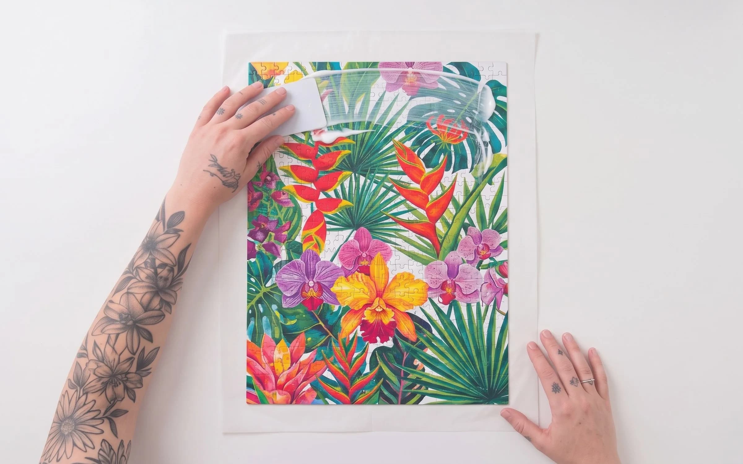 Mão espalhando cola sobre o quebra-cabeça floral usando um cartão de plástico.